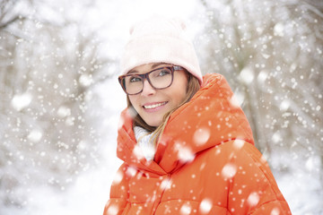  Woman in snowfall. Close-up portrait shot of a happy middle aged female wearing hat while standing outdoor and enjoy snowfall. 