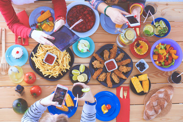 Top view of group of people having dinner together while sitting at wooden table. Food on the table. People eat fast food.