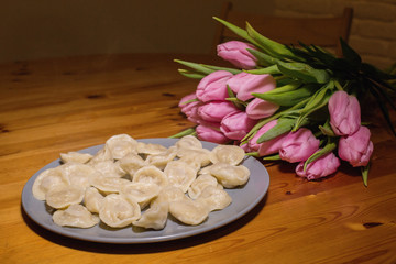 dumplings and a bouquet of pink tulips on a wooden background. tasty and strange feeding to a woman.