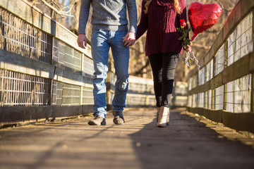 Couple walking holding hands no faces. She holds a red balloon and a red rose.