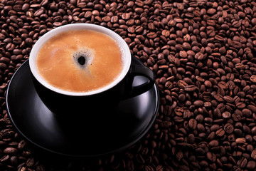 Black coffee cup and saucer one single for espresso or capuccino filled full of coffee beans on a background of scattered dark coffee beans photo 