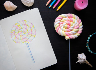 Candy illustration and candy on stick. Artist workplace with sketch book top view photo.