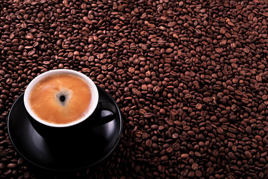 Black coffee cup and saucer one single for espresso or capuccino filled full of coffee beans on a background of scattered dark coffee beans photo 
