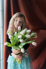 Adorable Caucasian blond girl with bouquet of tulip  flowers on brown background