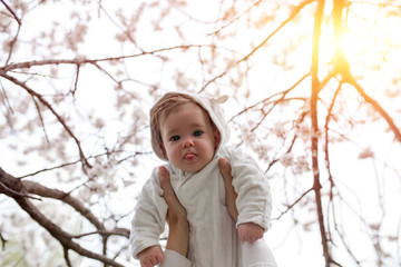 Happy family. mother hands throws up child in the blooming apple trees, on sunny day in the park.