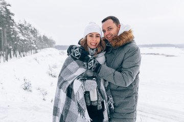 Fototapeta na wymiar Happy pair of male and female embracing and having fun wearing warm clothes outside on coast behind