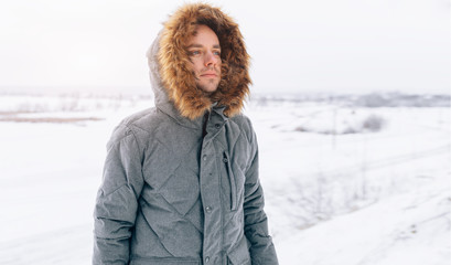 man wearing gray winter jacket with hood on in winter snow