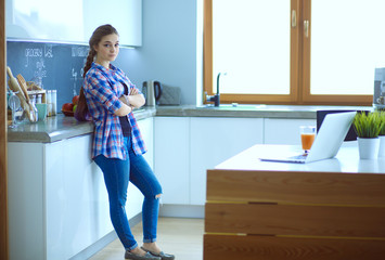 Portrait of young woman standing with arms crossed against kitchen background.