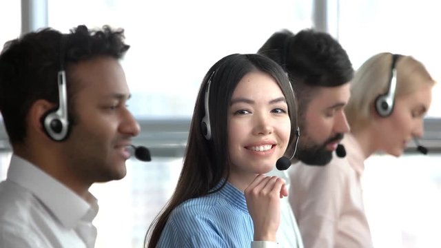 Asian girl in call center flirting. Asian tech support worker cheerfully smiling. Young asian girl turning head.