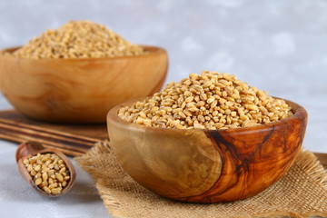 Dry pearl barley in a wooden bowl on a gray concrete table.