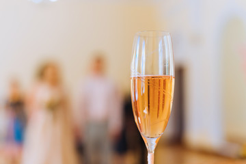 Close-up of a glass of champagne and in the background a guy and a girl who hold hands