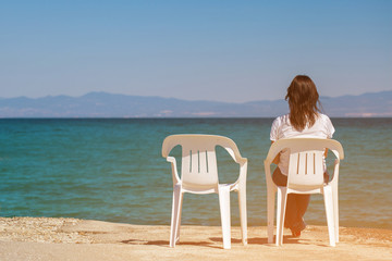 Girl sitting on white chair near the blue sea. Woman looking int