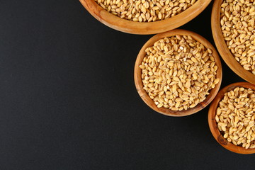 Dry pearl barley in a wooden bowl on a black chalkboard.