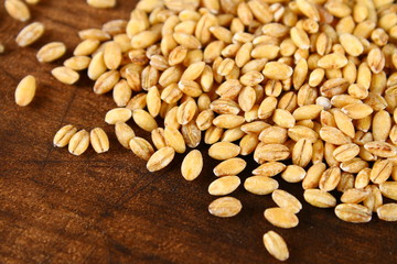 Dry pearl barley with a handful on a wooden table.