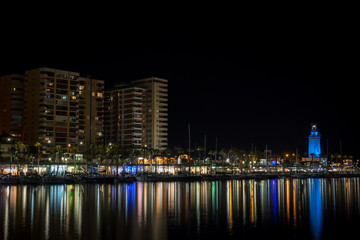 Fototapeta na wymiar View of Malaga city and lighthouse and their reflections on water from harbour, Malaga, spain, Euope at night