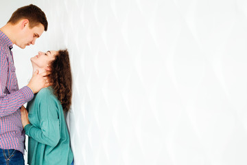 a gentle photo of a guy and his girlfriend who look to each other near white wall