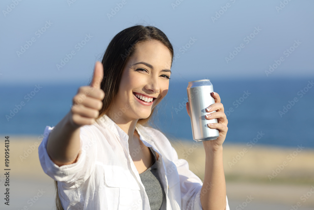 Wall mural Woman holding a refreshment can looking at you on the beach