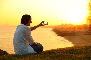 Woman taking photos with a smart phone at sunset