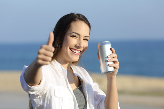 Woman holding a refreshment can looking at you on the beach
