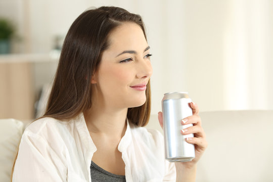 Woman holding a soda can looking away at home