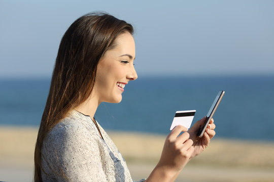 Woman paying on line with credit card on the beach