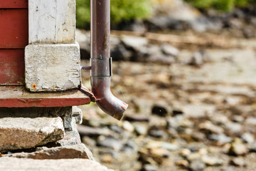 Thin drainpipe on cottage wall, rocks background
