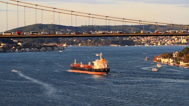 Tanker ship passing under the FSM Bridge with a heavy car traffic on the bridge. Aerial view on sunset in Istanbul, Turkey