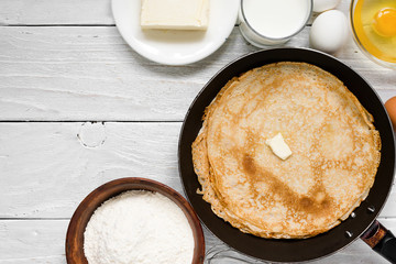 Stack of pancakes with butter on frying pan with ingredients on white table