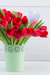 Fresh red tulip flowers bouquet on shelf in front of wooden wall.