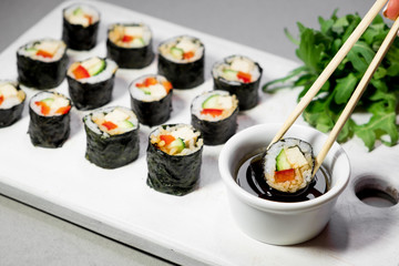Vegan sushi rolls with quinoa, vegetables and soy-nut sauce on a white plate, light background. Vegan Healthy Food Concept.