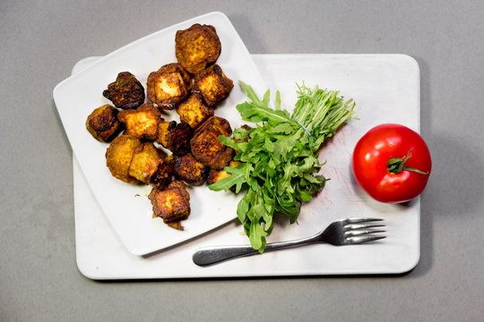 fried Indian slices of cottage cheese on a plate with tomato and rocula