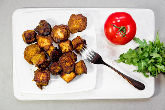 fried Indian slices of cottage cheese on a plate with tomato and rocula