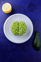 Avocado and lemon, pasting of sandwiches with avocado on a white plate on the ultraviolet background, green spread made with avocado, half a lemon, vegetarian food, healthy food, Mexican food