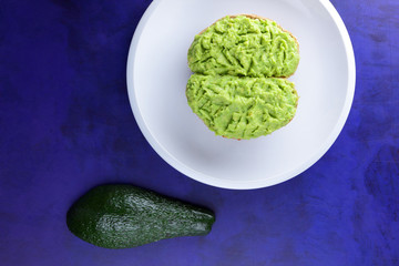 Avocado and lemon, pasting of sandwiches with avocado on a white plate on the ultraviolet background, green spread made with avocado, half a lemon, vegetarian food, healthy food, Mexican food