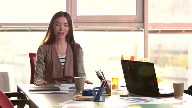 Woman putting cap on pen, windows backround. Sitting asian woman finished her office work and go away.