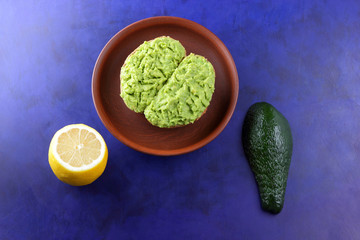 Avocado and lemon, pasting of sandwiches with avocado on a clay plate on the ultraviolet background, green spread made with avocado, half a lemon, vegetarian food, healthy food, Latin American cuisine