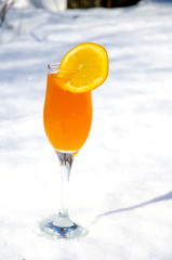 
A glass filled with orange juice stands on the snow.