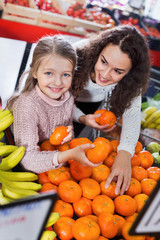 Mother and small pretty daughter buying  citrus fruits
