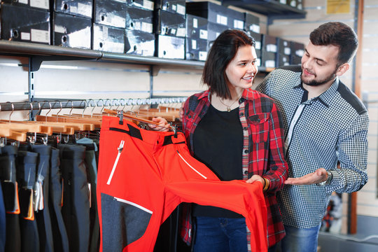 Young couple choosing touristic trousers in sports clothes store