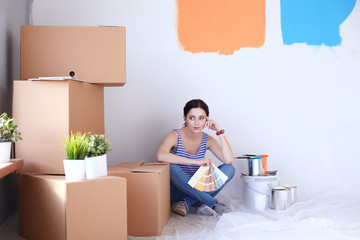 Woman choosing paint colour from swatch for new home sitting on wooden floor. Woman in the house