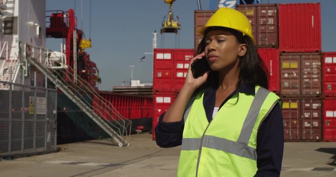 An attractive female worker talking on a mobile phone at a busy shipyard. Shot on RED Epic.