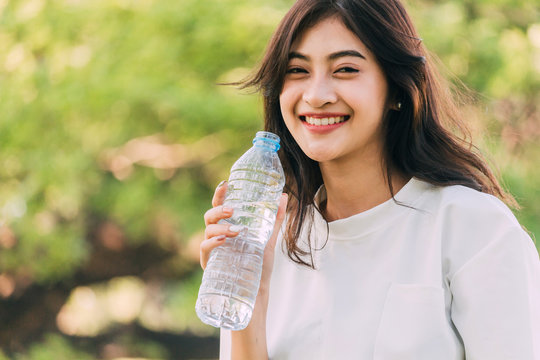 Beautiful woman drinking water at summer green park. Healthy lifestyle concept