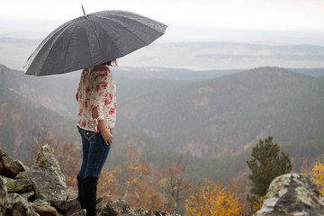 Caucasian Young woman looking over scenic view with umbrella in the rain