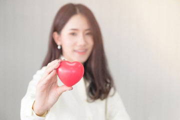 Attractive young asian beautiful woman smiling, happy face and holding red love hearts shape concept for valentine's day and health care. (Selective focus on heart shape and blurred background)