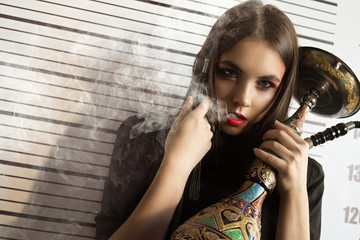 Obraz premium Portrait of a girl model in a stylish image on a background with a smoking peg in her hands. Fashion, style, beauty, portrait.