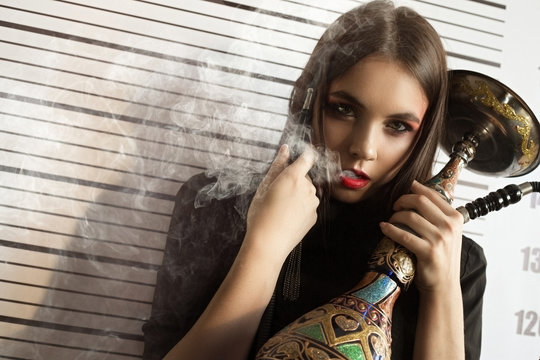 Portrait of a girl model in a stylish image on a background with a smoking peg in her hands. Fashion, style, beauty, portrait.