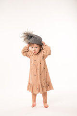 Portrait of happy little girl. Cute little girl in beige dress in a gray hat isolated on white background.