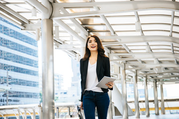 Beautiful young businesswoman walking outside public transportation station. Businesswoman traveler with suitcase on the way to the airport.