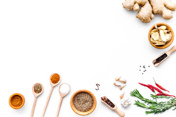 Colorful dry spices in bowls and spoons near ginger, garlic, rosemary on white background top view copy space