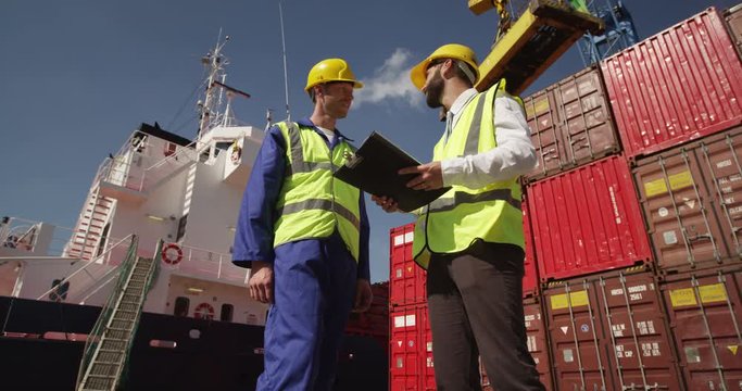 Dock workers discuss logistics at the harbor amidst shipping industry activity. Shot on RED Epic.